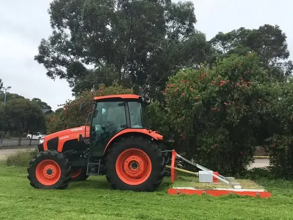 Orange tractor with a slasher attached, parked on mown grass